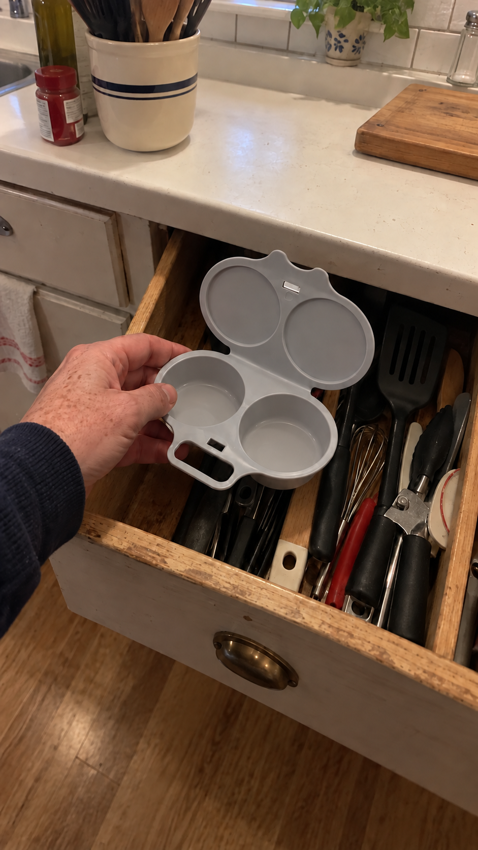 Illustrative scene: a person putting the gray maker in a kitchen drawer under uneven household light